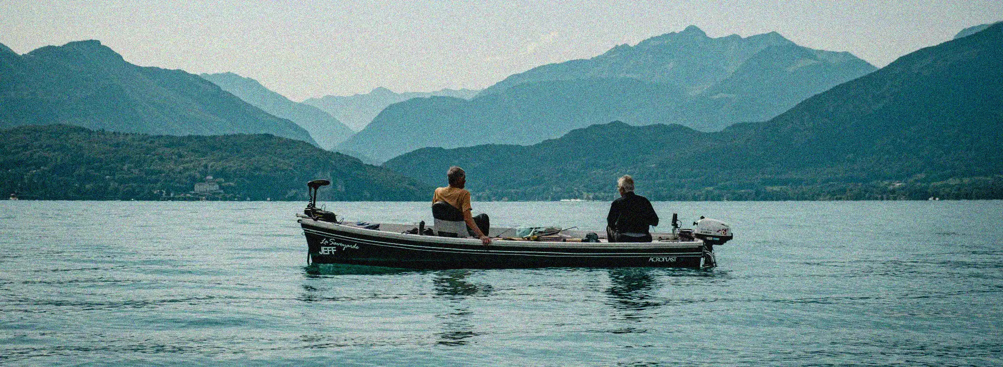 Two people on a boat in a lake with mountains in the background